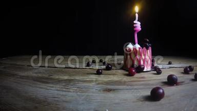 一支燃烧着的蜡烛在一张老式木桌上的一个喜庆的粉红色纸杯蛋糕上燃烧着。 手拿起蜡烛。 在黑色的